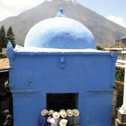 Admirers look in on Maximón from the side window of his chapel in the churchyard, which he occupies for only a few days per year. Volcán San Pedro towers in the distance across the bay of Santiago. (photo: Victoria Stone)