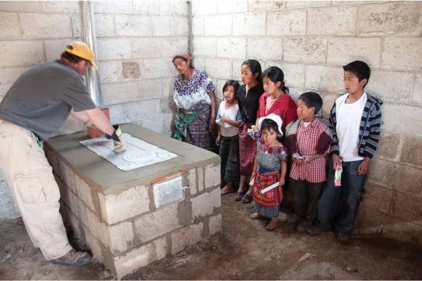A Guatemalan family watches the finishing touches put on their new efficient stove with chimney pipe